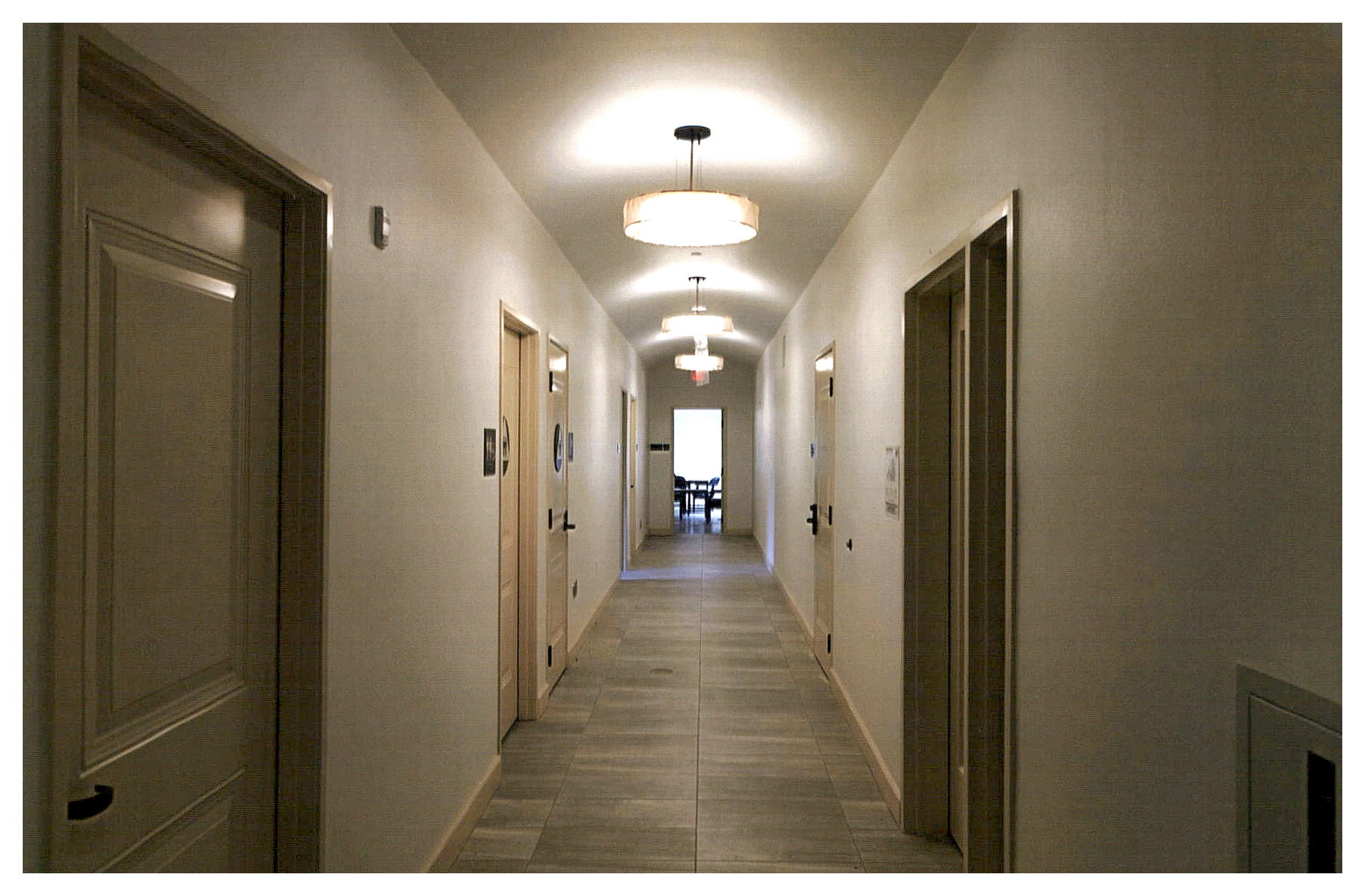 After: view of another hallway with wide cylindrical pendant light fixtures suspended from a slightly arched ceiling.