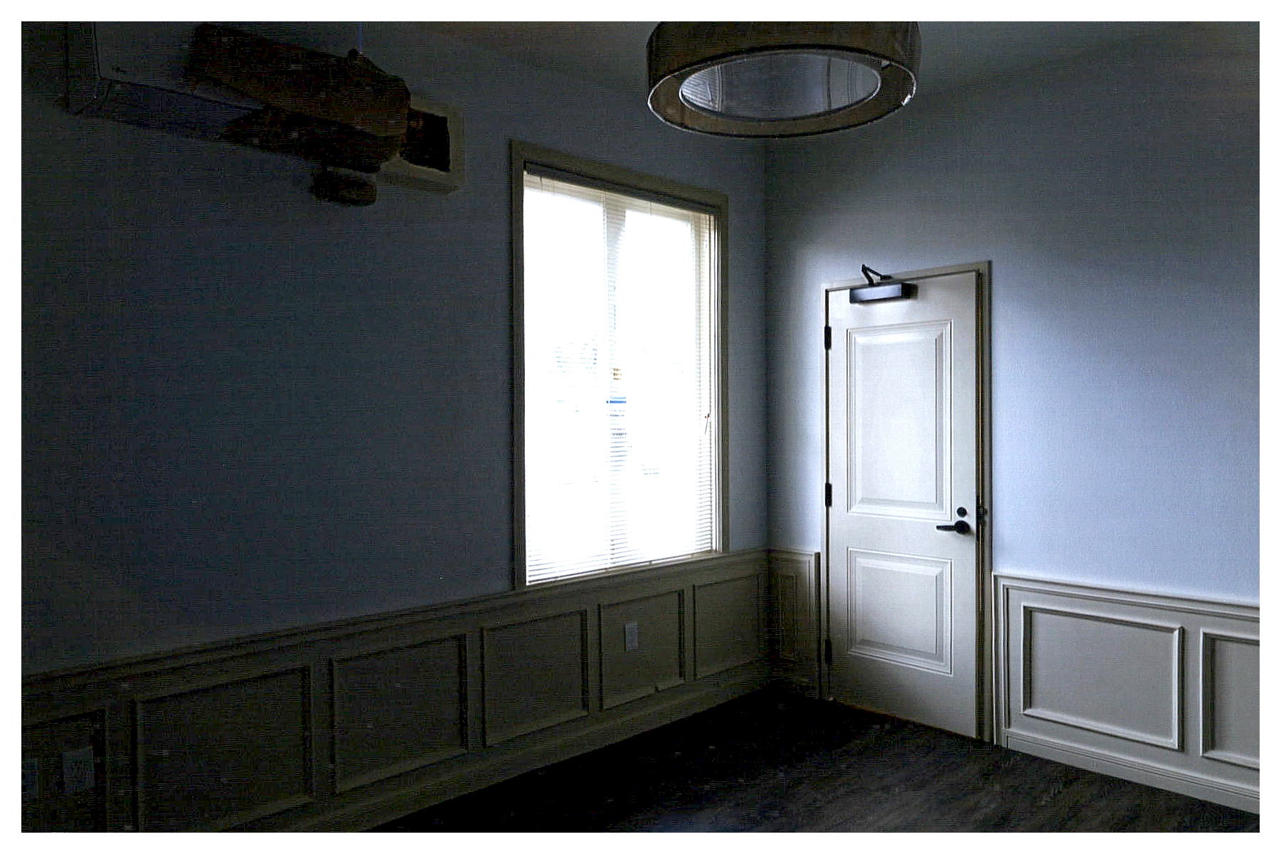 After: corner view of renovated room with a rehabilitated window, entrance door with closer, restored paneled wainscoting and new pendant light fixture.