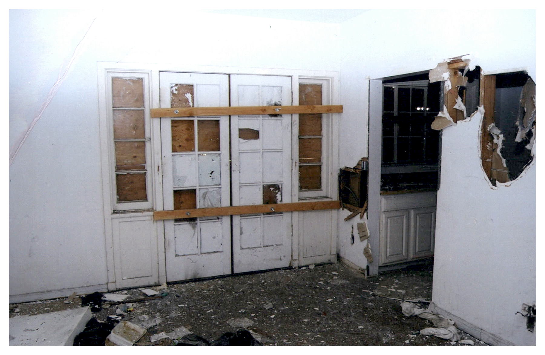 Before: same interior view of apartment with paired french doors boarded up and wall damage.