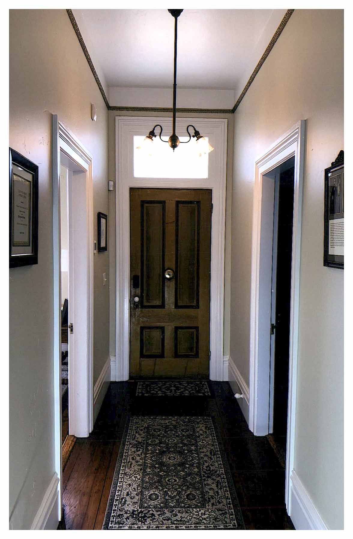 After: interior view of front entrance at end of narrow hall showing refinished wood floor and light-colored interior paint that fills the hall with light from transom.