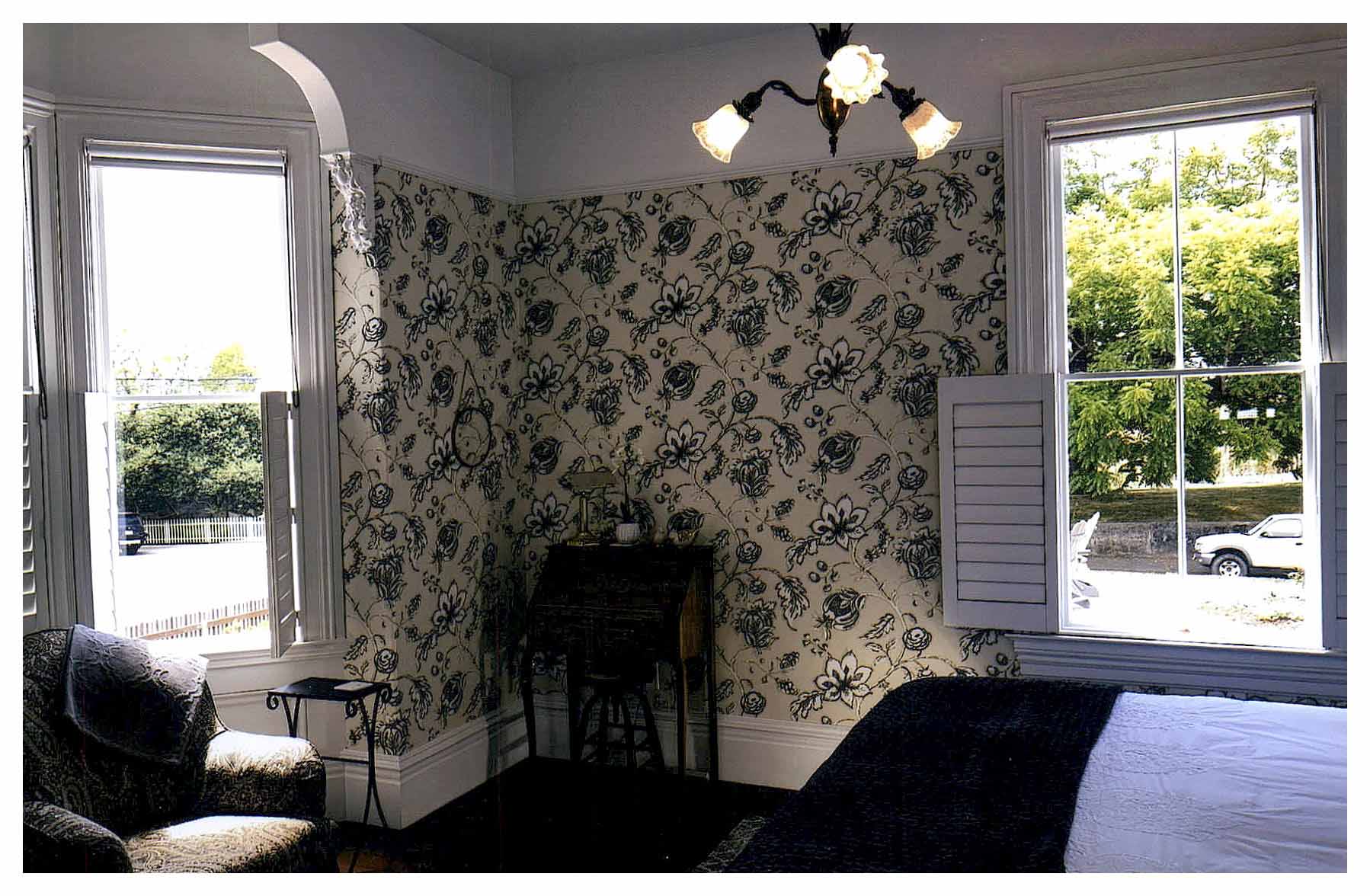 After: bedroom showing another bay window in an arched alcove finished with patterned wallpaper up to the picture rail.