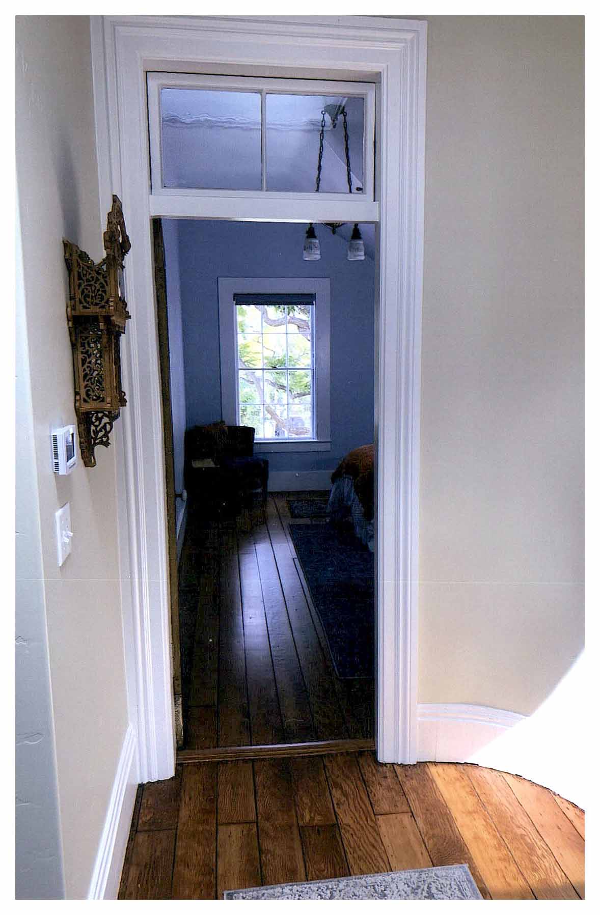 After: view at end of second floor hallway showing the door and transom of another bedroom adjacent to a unique rounded corner. Hallway walls are a light cream color.