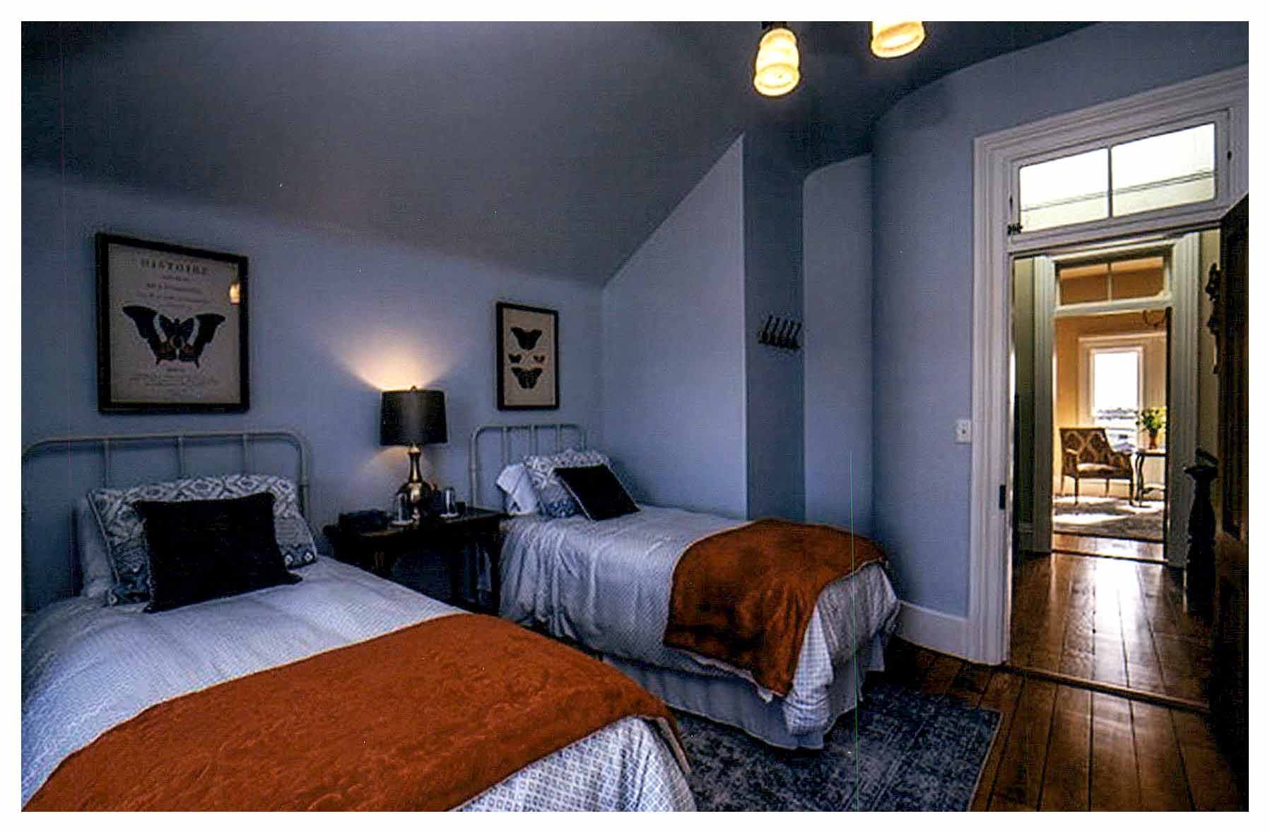 After: second floor bedroom facing door with transom to hallway and other side of the rounded corner. Light blue walls and sloped ceiling compliment white painted trim and refinished wood floor.