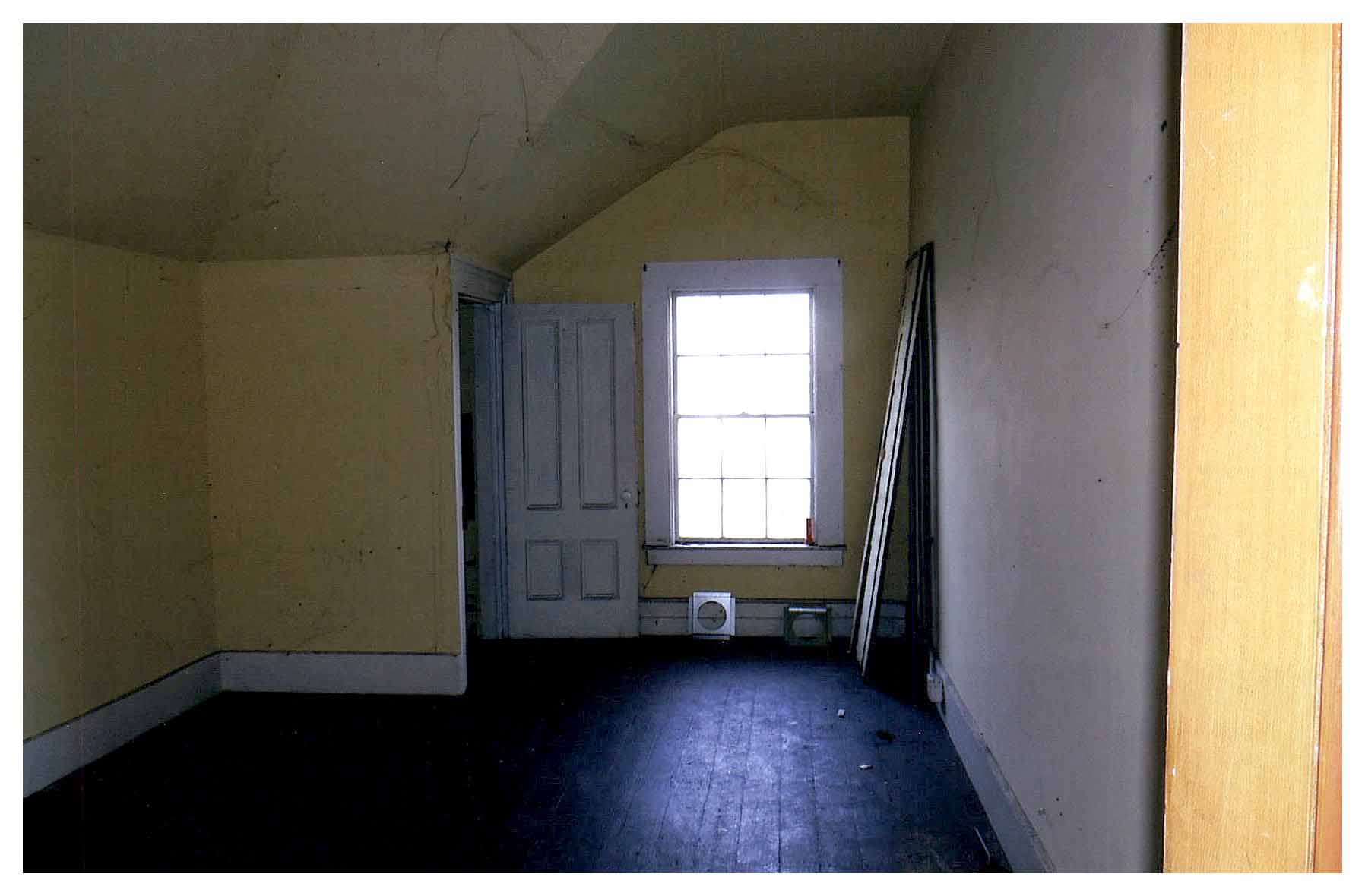 Before: same view of bedroom with unfinished floors, light yellow walls and a white sloped ceiling.