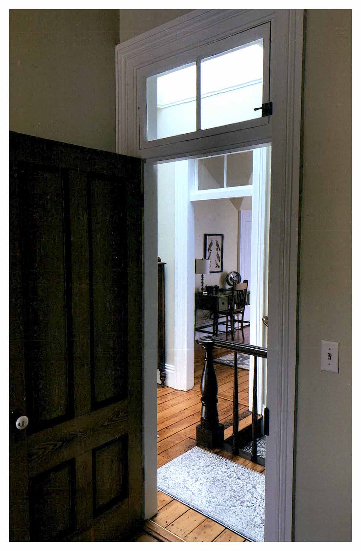 After: close-up of bedroom door and transom with view of hallway and bedroom beyond. Light colored surfaces and large skylight brighten the entire second floor.