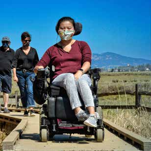 Woman using boardwalk in a wheelchair while masked for COVID-19