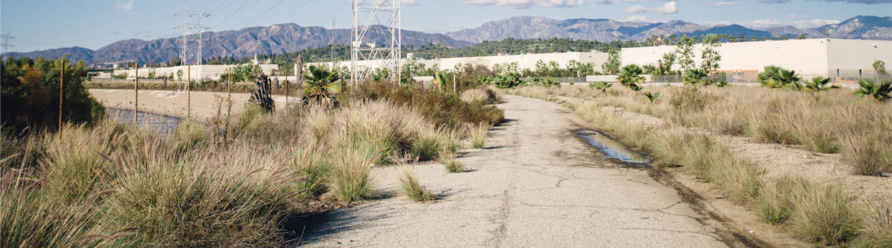 The Bowtie looking north. A paved road with industrial buildings in the background and the San Gabriel Mountains in the far distance.