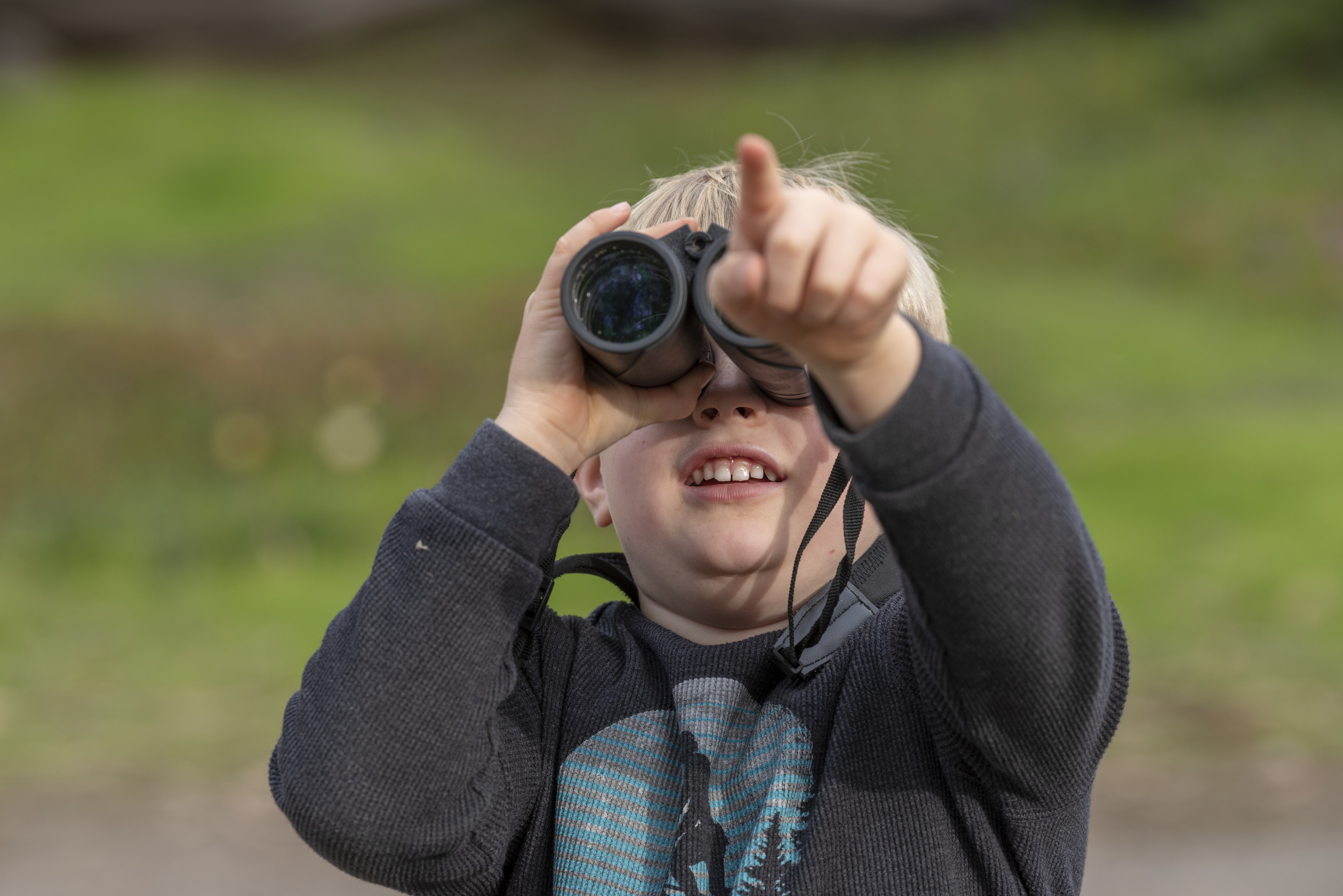 Young child looking through binoculars pointing in nature