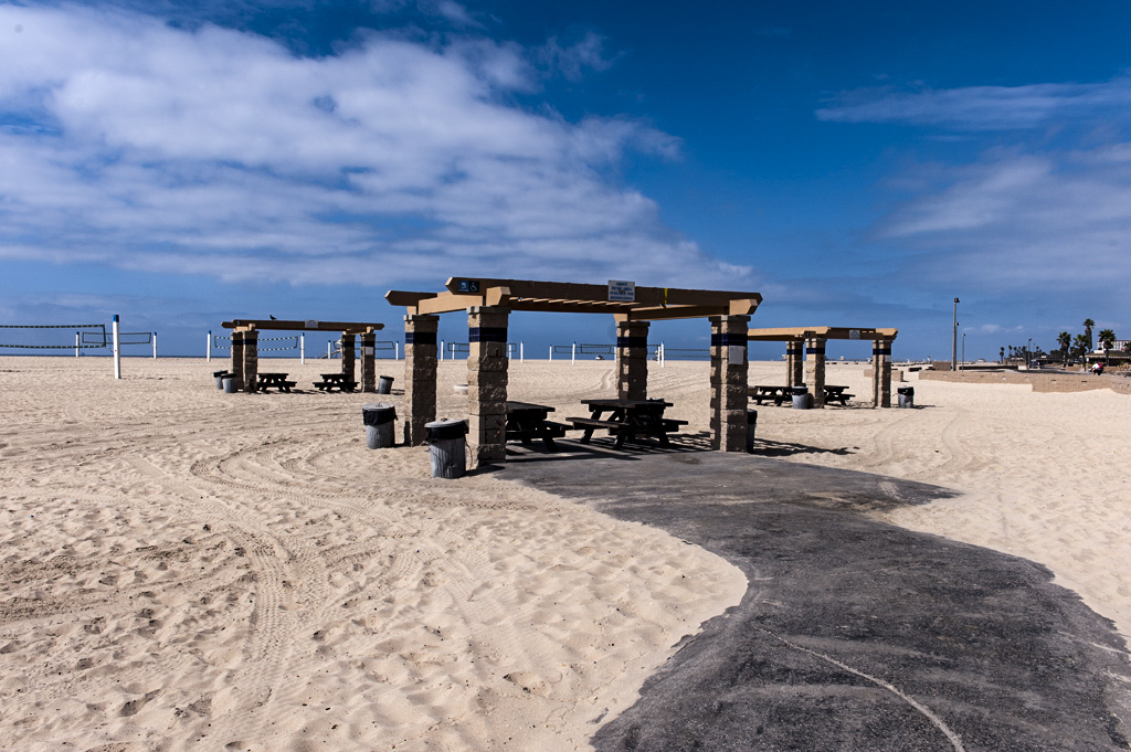Ramada with a picnic bench and a fire ring sit on the sand.
