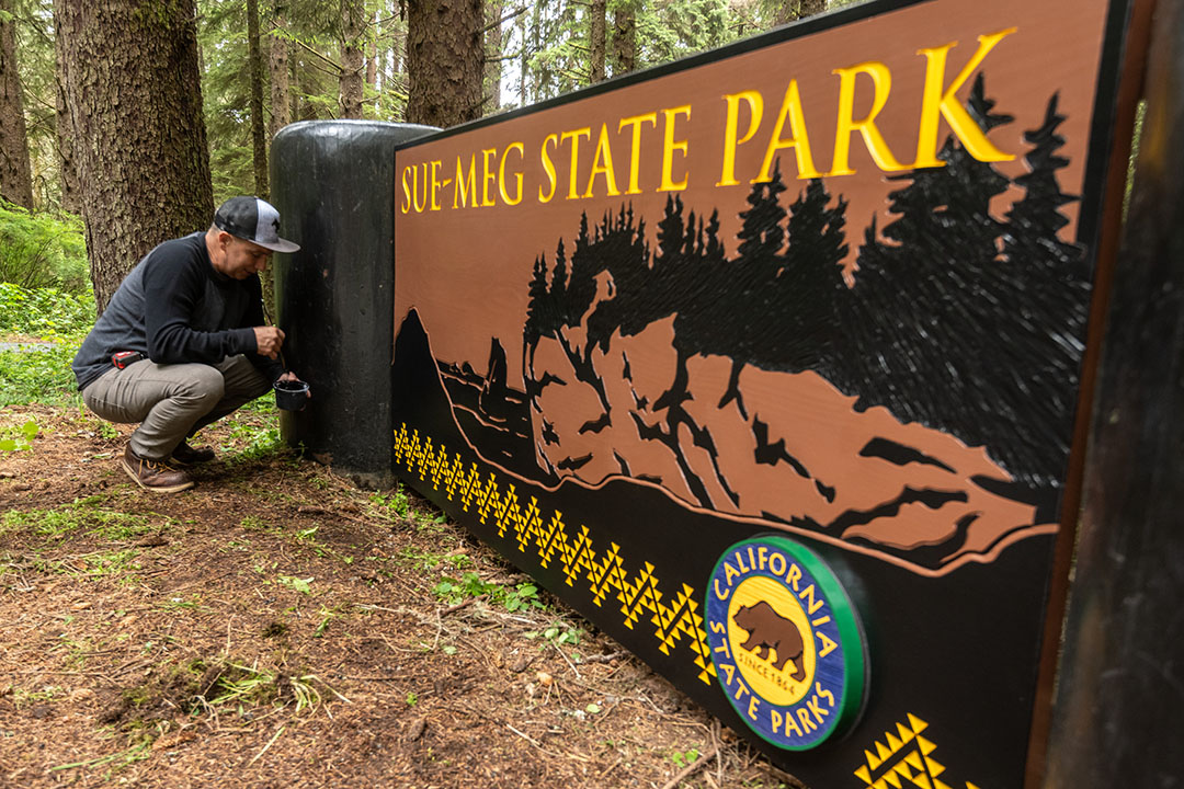Sign Carver Alme Allen, a local artist of Karuk and Yurok descent who was hired to redesign the signs, puts the finishing touches on the new Sue-meg State Park sign June 2022